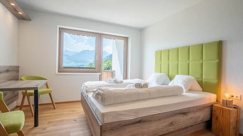 Helles Schlafzimmer mit Holzboden, grünem Kopfteil und Bergblick durch das große Fenster.