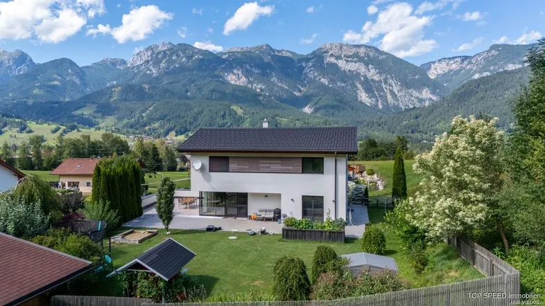 Modernes Einfamilienhaus mit großem Garten und beeindruckendem Bergblick im Hintergrund.