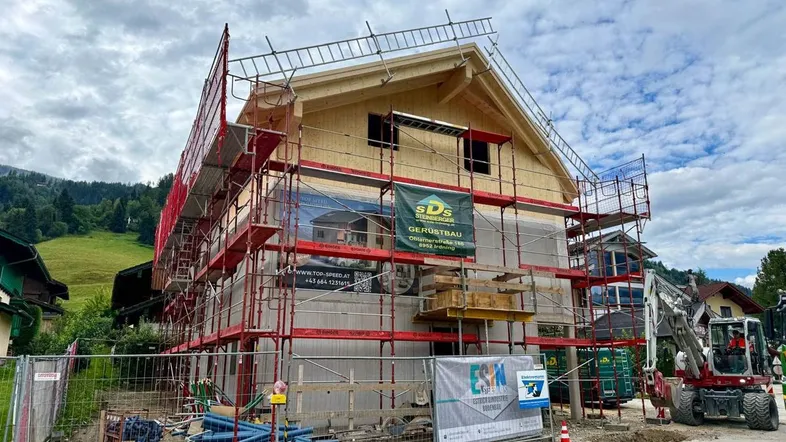 Neubau eines Hauses im Rohbau mit Gerüst und Bergblick in ländlicher Umgebung.