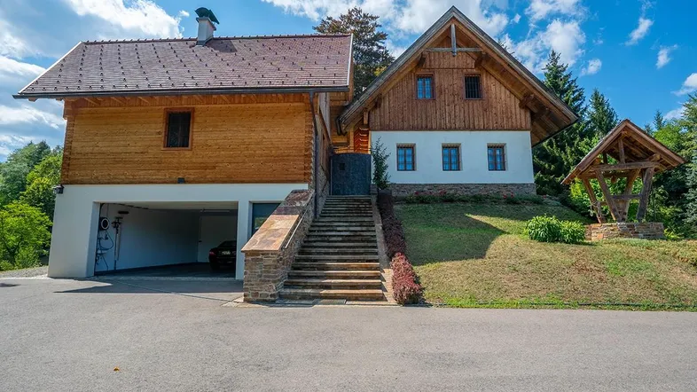 Traditionelles Landhaus mit Holzfassade, Steintreppe und integrierter Garage unter blauem Himmel.