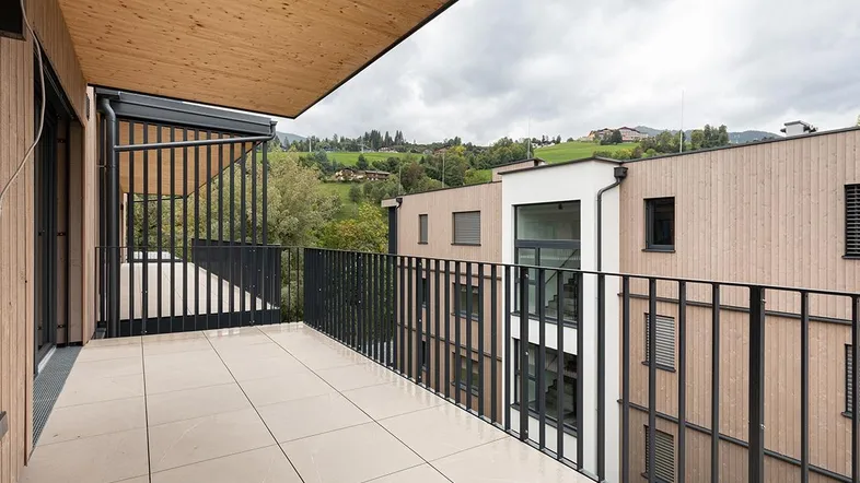 Geräumiger Balkon mit Fliesenboden und Holzdecke, bietet einen weiten Blick auf die umliegende Landschaft und moderne Gebäude.