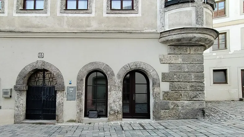Historische Fassade eines Gebäudes mit Rundbogenportalen und Steinverzierungen an einer gepflasterten Straße.