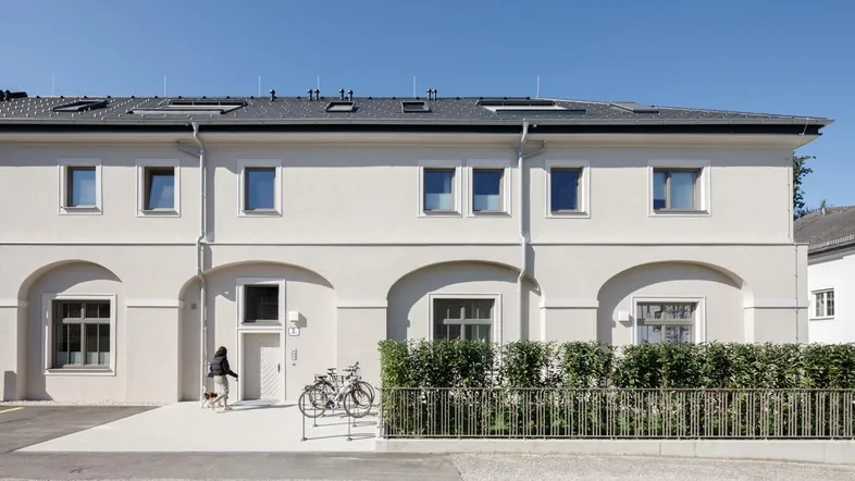 Modernes Mehrfamilienhaus mit heller Fassade, großen Fenstern und gepflegter Hecke.