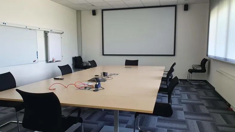 Geräumiger Konferenzraum mit großem Tisch, Projektionsfläche und Whiteboards für Besprechungen.