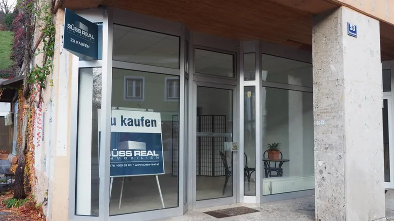 Außenansicht eines Geschäftsgebäudes mit großen Fenstern und einem 'Zu Kaufen'-Schild.