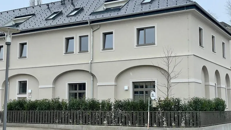 Modernes Gebäude mit heller Fassade, Dachfenstern und gepflegter Hecke im Vorgarten.