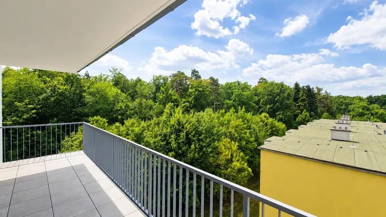 Geräumiger Balkon mit Fliesenboden und weitem Blick ins Grüne und auf umliegende Gebäude.