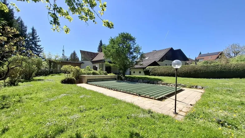 Großer Garten mit Rasenfläche und überdachtem Pool, umgeben von Bäumen und Grünflächen.