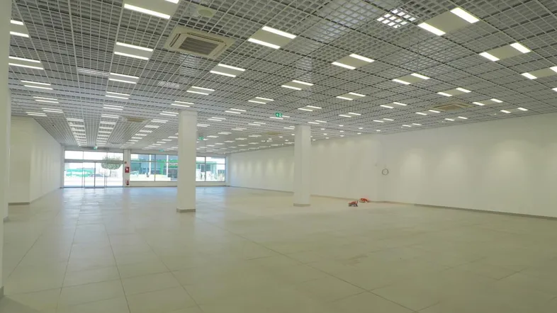 Großer, leerer Gewerberaum mit Fliesenboden, Rasterdecke und großen Fenstern.