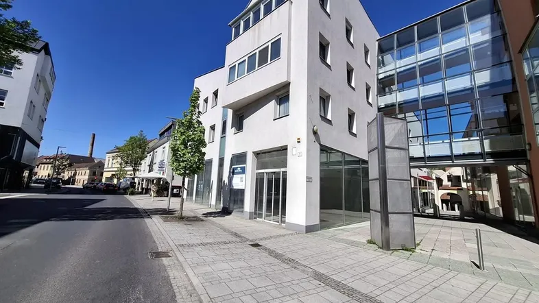 Modernes Geschäftsgebäude mit großen Schaufenstern und klarem Himmel an einem sonnigen Tag.