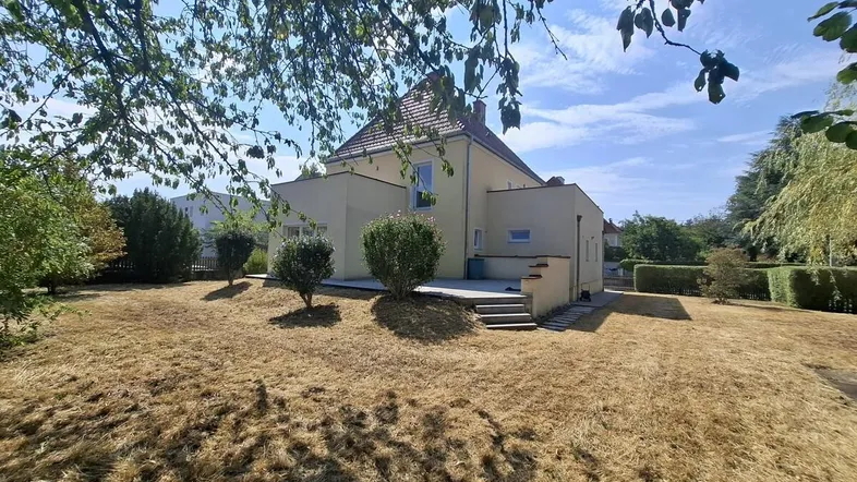 Großzügiges Einfamilienhaus mit weitläufigem Gartenbereich unter blauem Himmel an einem sonnigen Tag.