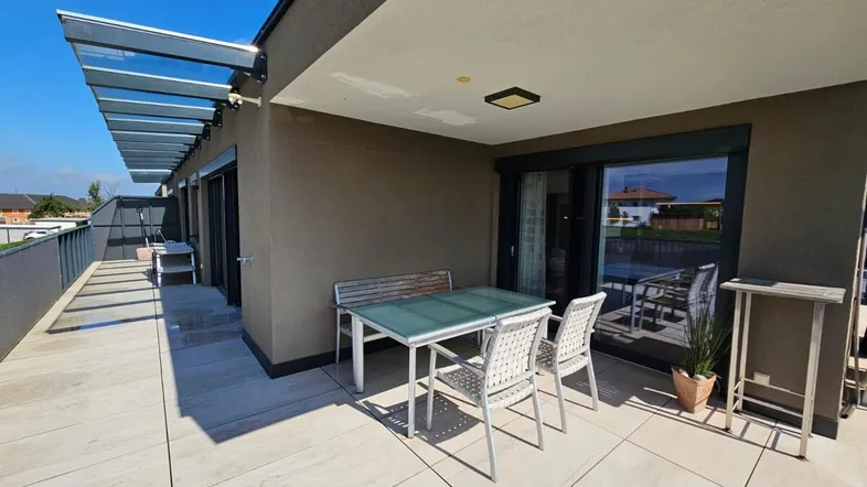 Geräumige Dachterrasse mit modernen Fliesen, Esstisch und schützender Überdachung für sonnige Tage.