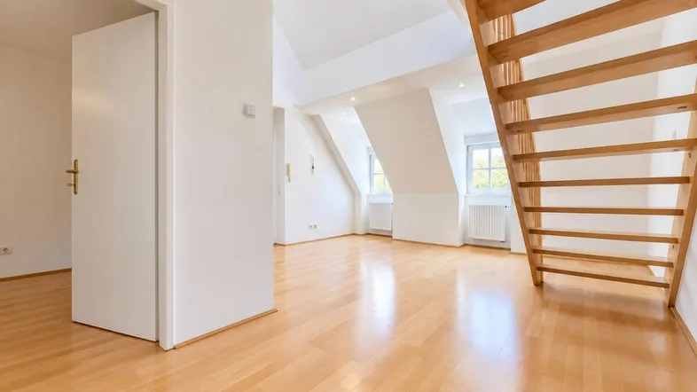 Helles Dachgeschosszimmer mit Holztreppe, Parkettboden und schrägen Wänden.