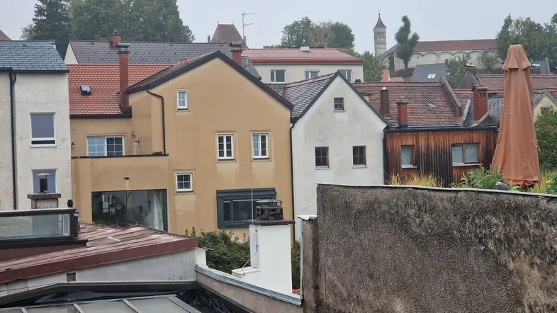 Blick über die Dächer einer Stadt mit verschiedenen Gebäuden und einem Kirchturm im Hintergrund.