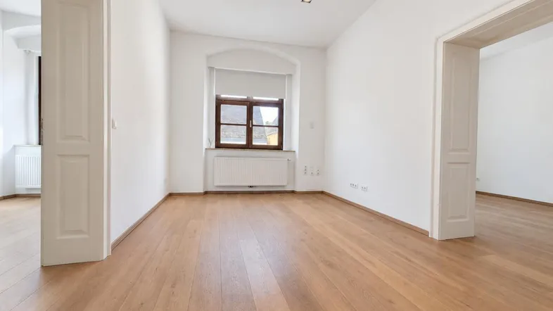 Heller, leerer Raum mit Holzboden, weißen Wänden und einem Fenster mit Holzrahmen, bereit zur Einrichtung.