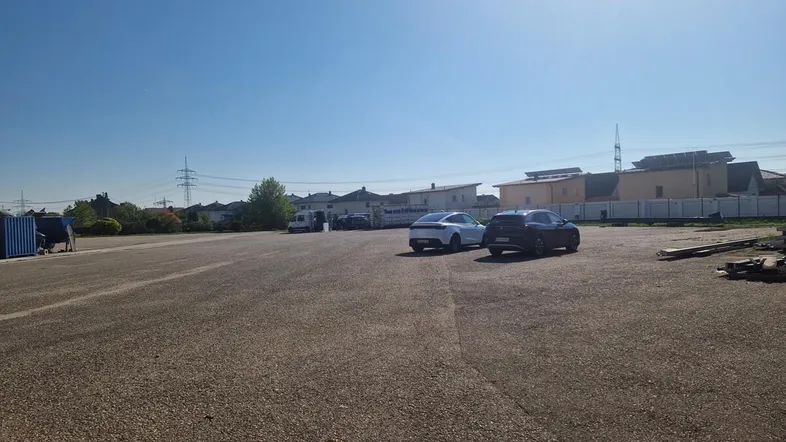 Großer, asphaltierter Außenbereich mit parkenden Autos und Gebäuden im Hintergrund unter klarem Himmel.