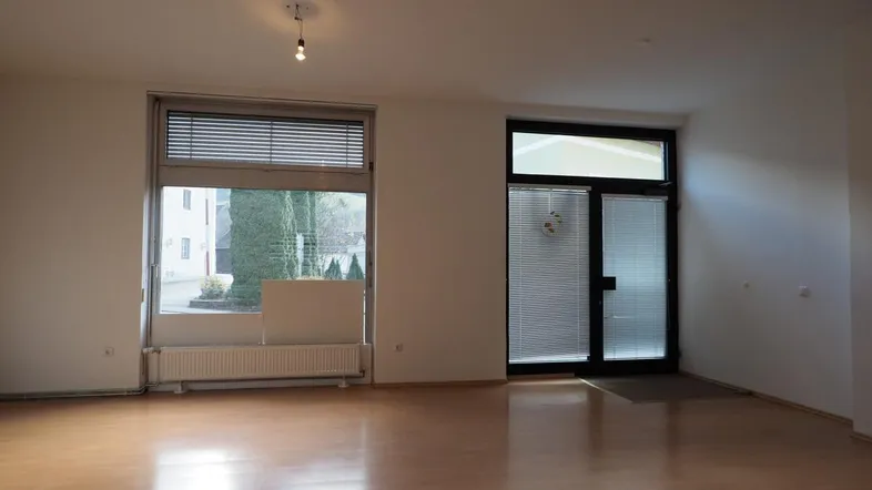 Heller, leerer Raum mit Holzfußboden, großen Fenstern und einer Glastür, ideal für ein Geschäft.