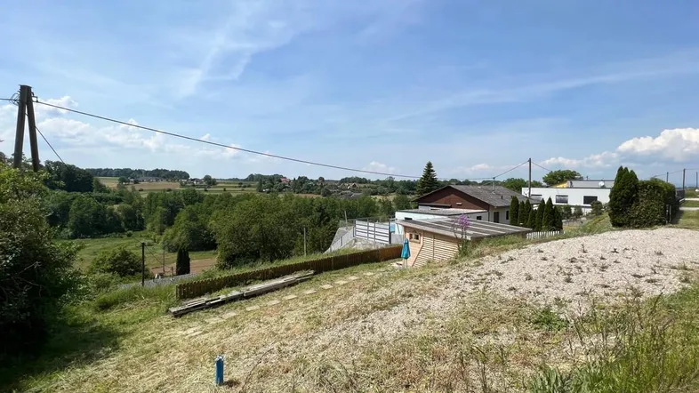 Ländliche Umgebung mit weitem Blick über Felder, Bäume und vereinzelte Häuser unter blauem Himmel.