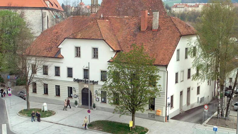 Traditionelles Gebäude mit weißer Fassade und roten Ziegeldächern an einer belebten Straßenecke.