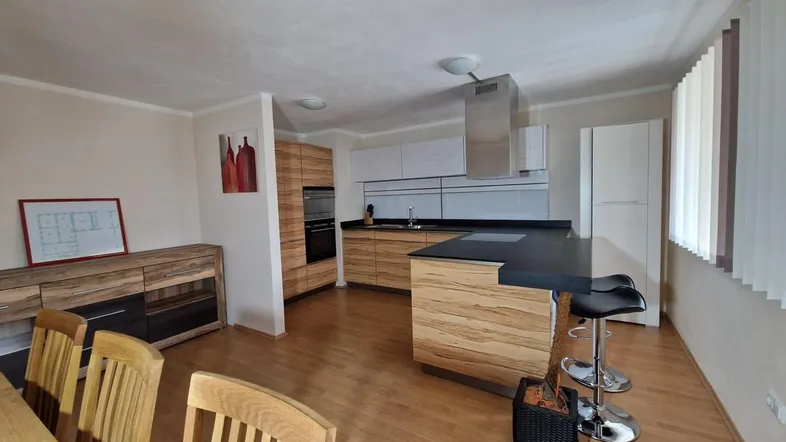 Moderne offene Küche mit Holzelementen, dunkler Arbeitsplatte und integrierten Geräten in einem hellen Raum.