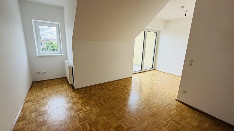 Helles Zimmer mit Parkettboden, Dachschräge und Zugang zu einem Balkon, ideal als Schlafzimmer.