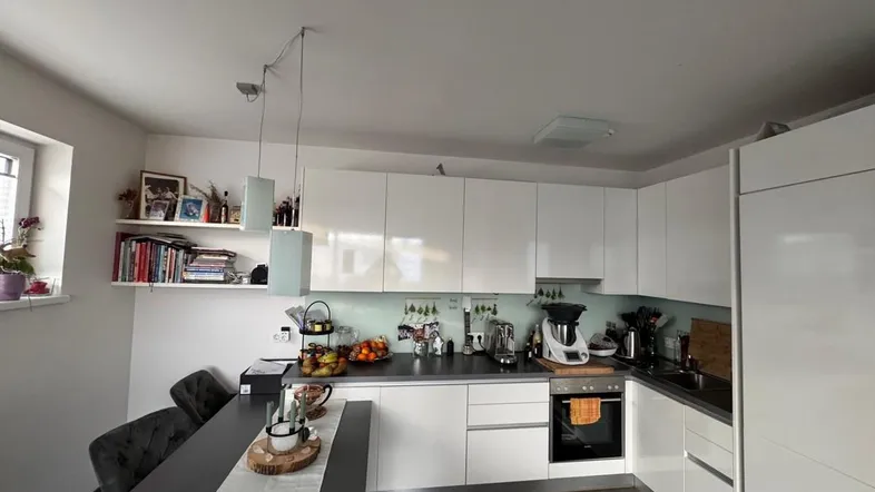 Moderne Küche mit weißen Hochglanzfronten, dunkler Arbeitsplatte und integriertem Backofen.