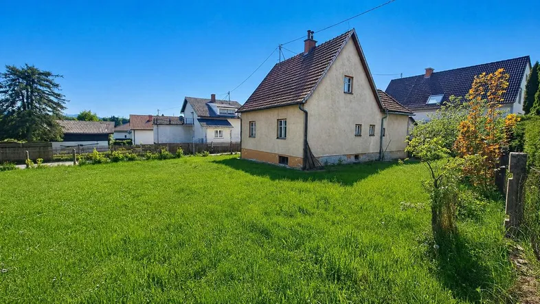 Seitenansicht des Hauses mit großem, sonnigen Rasengrundstück und Bäumen.