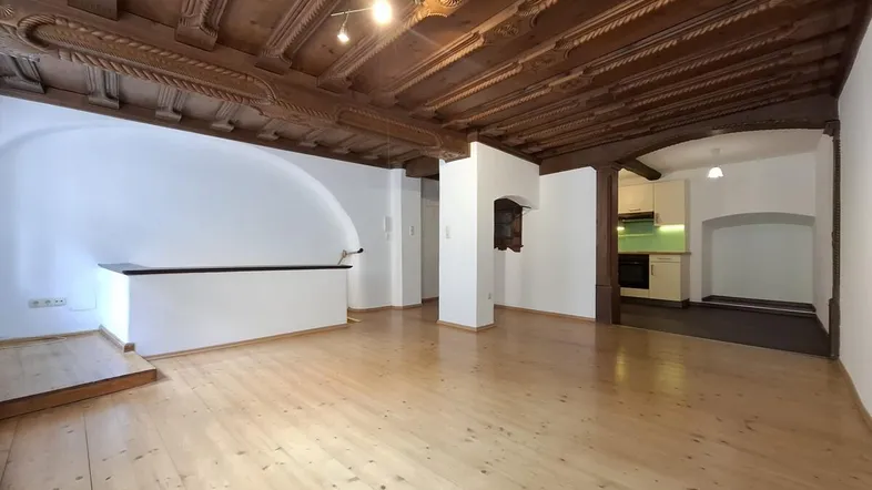 Geräumiges Wohnzimmer mit beeindruckender Holzbalkendecke und hellem Holzboden.