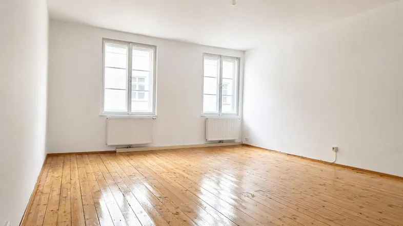 Helles Zimmer mit Holzdielenboden, weißen Wänden und zwei Fenstern, bereit zur Einrichtung.
