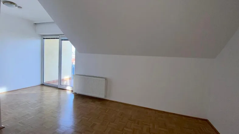 Helles Zimmer mit Parkettboden, Dachschräge und Zugang zu einem Balkon oder einer Terrasse.
