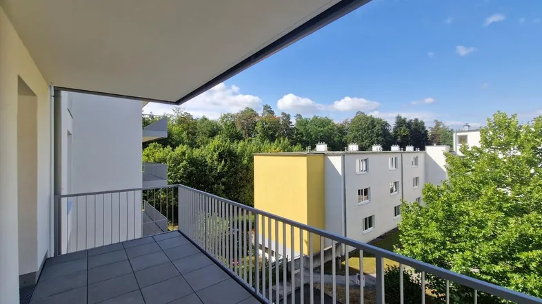 Geräumiger Balkon mit Fliesenboden und Blick ins Grüne sowie auf umliegende Gebäude.