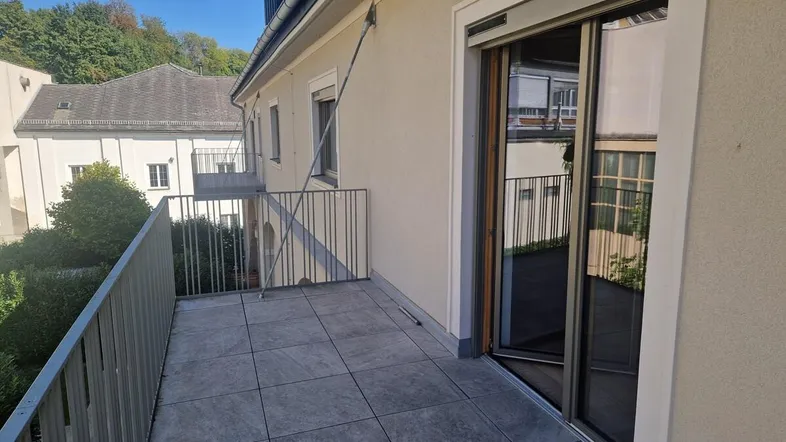 Geräumiger Balkon mit Fliesenboden und Blick auf die umliegenden Gebäude und Bäume.