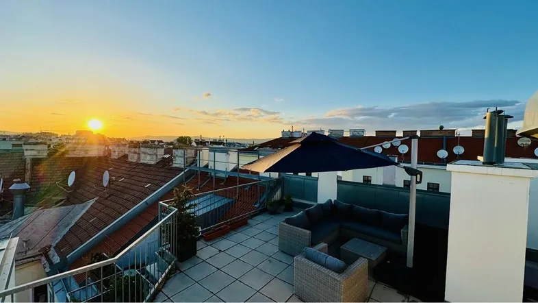 Große Dachterrasse mit bequemen Loungemöbeln und weitem Blick über die Stadt bei Sonnenuntergang.