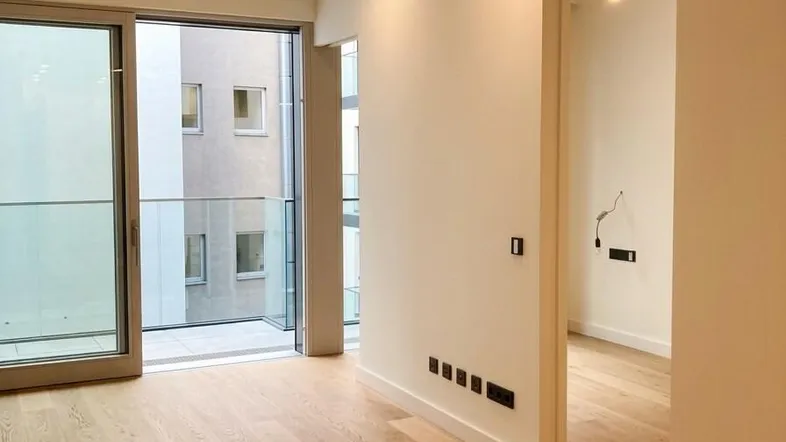 Helles Wohnzimmer mit Holzboden, großen Schiebetüren und Zugang zu einem Balkon.