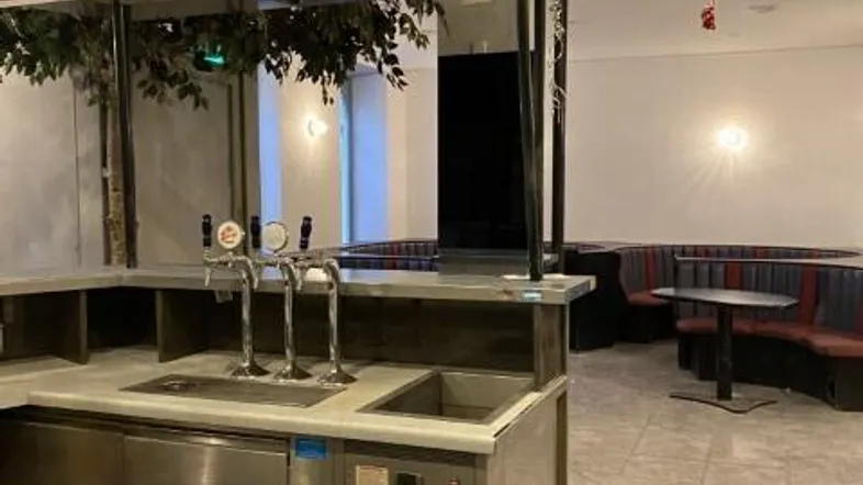 Moderner Barbereich mit Zapfanlage, gemütlichen Sitzgelegenheiten und dekorativen Kunstbäumen, bereit für Gäste.