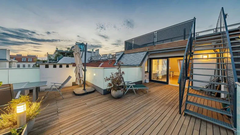 Geräumige Dachterrasse mit Holzboden, Sitzgelegenheiten und Blick auf die umliegenden Gebäude bei Sonnenuntergang.