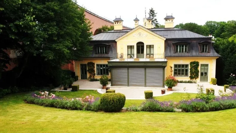 Rückansicht der Villa mit weitläufigem Rasen, blühenden Beeten und gepflegter Gartenanlage.
