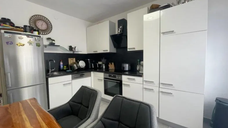 Moderne Küche mit weißen Schränken, dunkler Arbeitsplatte und integrierten Geräten.