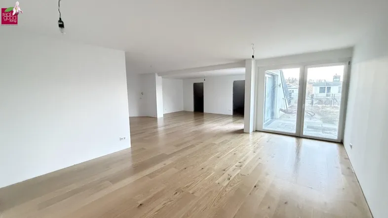 Geräumiges, helles Wohnzimmer mit neuem Holzparkettboden und Zugang zu einem Außenbereich.