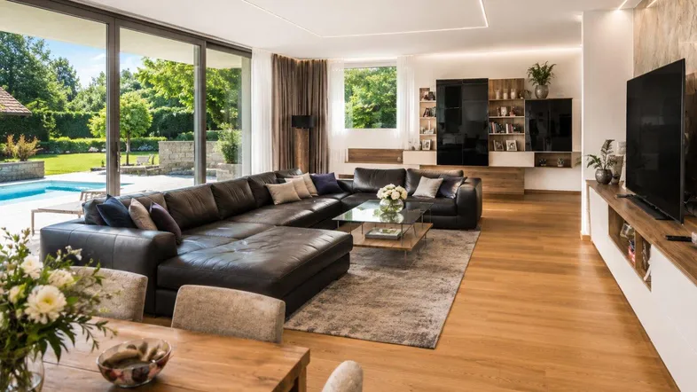 Helles Wohn- und Esszimmer mit großzügiger Ledercouch, Holzboden und Zugang zum Poolbereich.