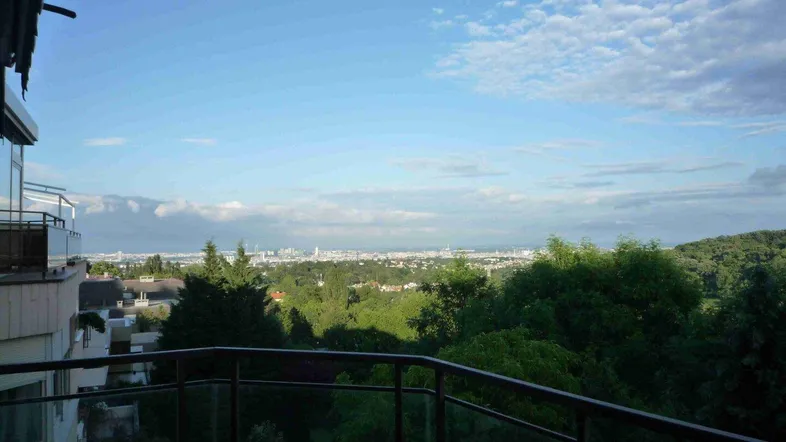 Geräumiger Balkon mit Glasgeländer bietet einen weiten Blick über die Stadt und grüne Umgebung.