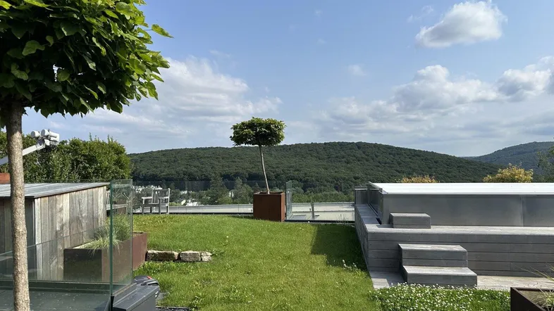 Großzügige Dachterrasse mit Rasenfläche, Whirlpool und weitem Blick über die bewaldeten Hügel.