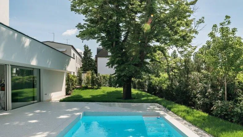 Moderner Außenpool mit klarem Wasser und umgebender Grünfläche unter blauem Himmel.