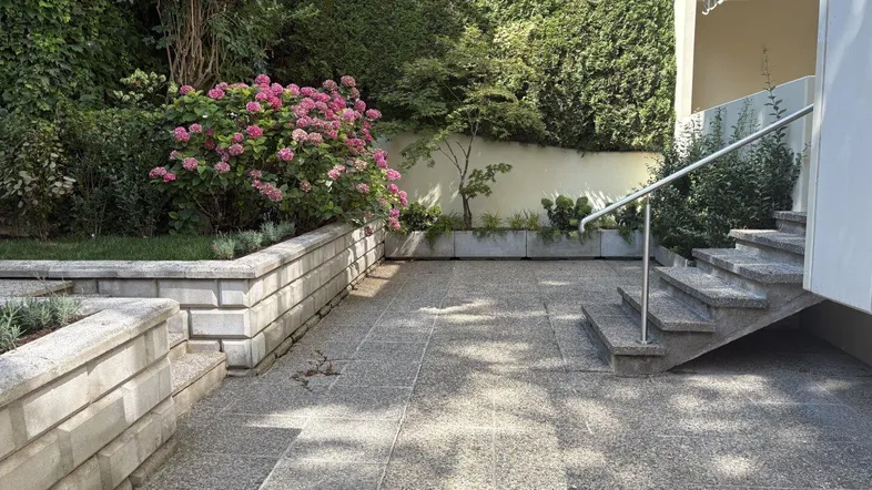 Gepflasterte Terrasse mit Stufen, umgeben von üppigem Grün und blühenden Hortensien.