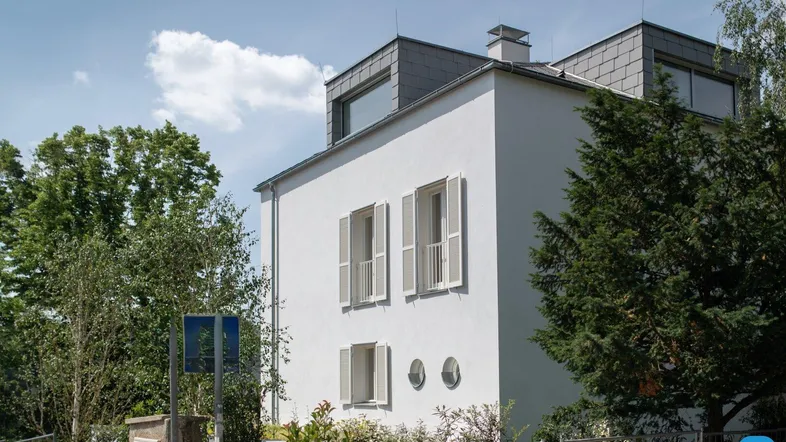 Seitenansicht eines modernen Wohnhauses mit weißer Fassade, Dachgauben und grüner Umgebung.