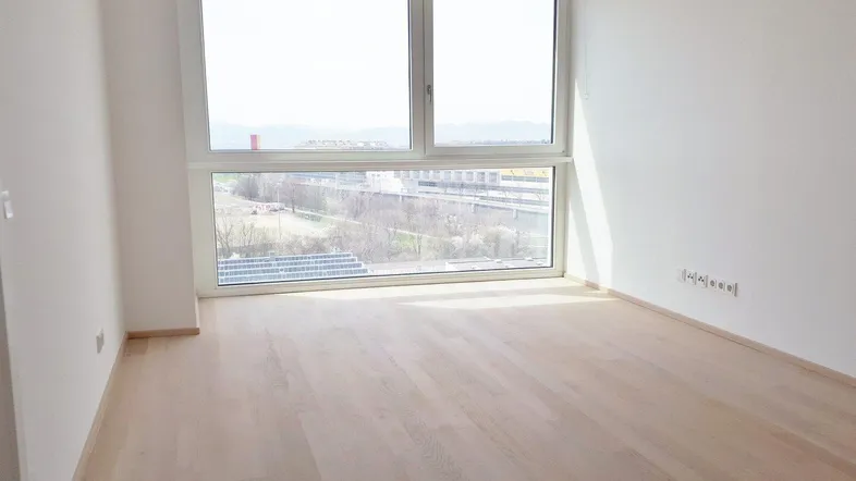 Helles Zimmer mit großen Fenstern und Parkettboden, bietet einen weiten Blick ins Grüne.
