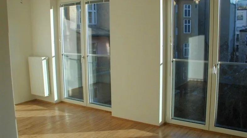 Helles Zimmer mit großen Fenstern, Holzboden und Heizkörper, ideal als Wohn- oder Schlafbereich.