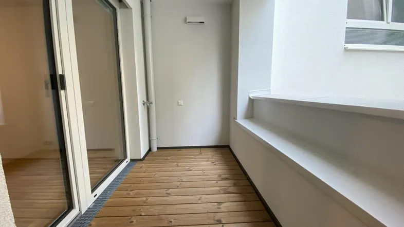 Heller Balkon mit Holzfußboden und großen Glasschiebetüren, ideal für entspannte Stunden im Freien.