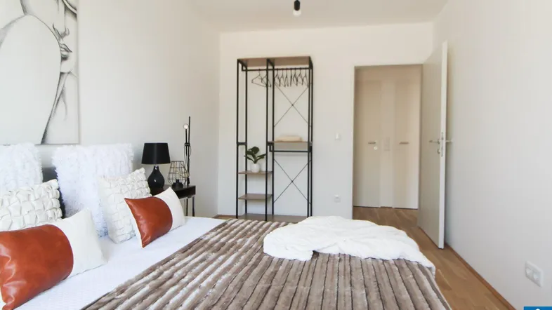 Modernes Schlafzimmer mit Holzboden, minimalistischem Kleiderständer und Kunstwerk über dem Bett.