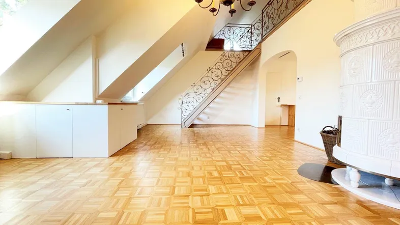 Geräumiges Wohnzimmer mit traditionellem Kachelofen, Parkettboden und einer eleganten schmiedeeisernen Treppe.